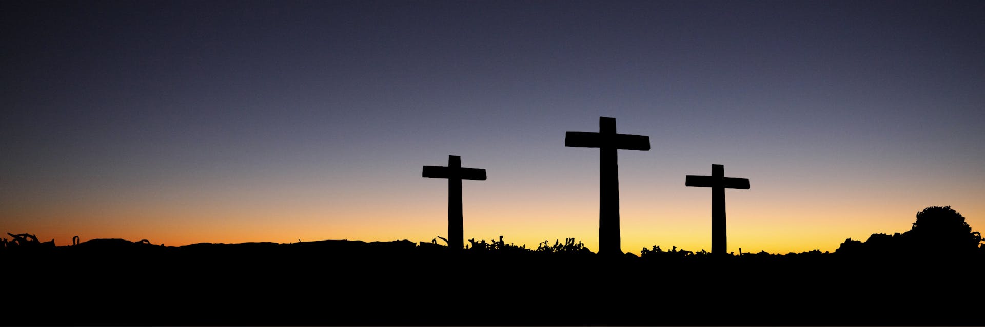 Three Christian crosses on a silhouette landscape with sunset.